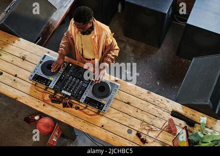 Above view of young African American male musician creating new music at lesire while touching turntables on dj set and mixing sounds Stock Photo