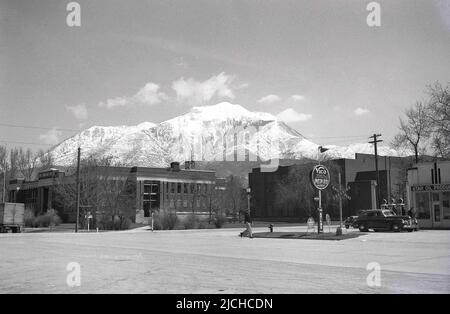 1930s, historical, a car of the era at at a gas station, Utah, USA, with the famous snow covered Wasatch mountains in the distance. A Rail road Crossing sign is on the forecourt, while the name Utah Oil Products is on the garage building. On the station sign the names Vico Motor Oil and Pep 88 gasoline, the oil and gas brands of the Utah Oil Refining Company. The first oil refinery in Utah, established in 1908, these brand names remained in use until 1948, when replaced by the brand name UTOCO. Other motor brands of the day seen; Atlas tyres & batteries & Quaker State motor oil. Stock Photo