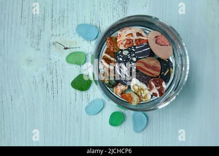 Amazing multi colored sea pebbles in glass goblet on blue wooden background Stock Photo