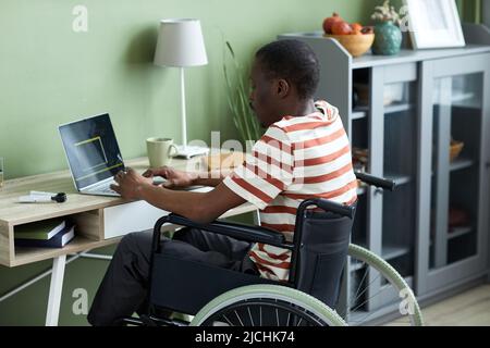 Side view portrait of black man in wheelchair using laptop and writing code while working from home Stock Photo