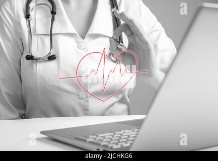 Doctor with ok gesture reporting electrocardiogram results to patient online using laptop. Remote medical consultation concept. Woman in lab coat sitting at table with computer. photo Stock Photo