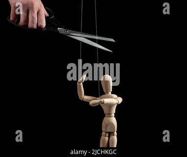 Hand with scissors cutting strings holding puppet. Independence, liberation from slavery, control, abuse cessation, successful recovery from addiction concept on black background. High quality photo Stock Photo