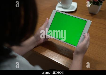 Woman using tablet with green screen mockup in living room view from behind the shoulder. Stock Photo