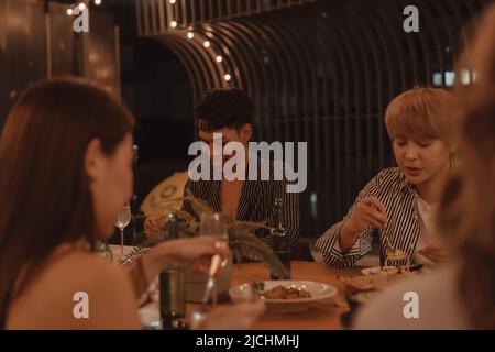 Young Asian friends eating and enjoying dinner together at outdoor restaurant. Friendship and reunion celebration Stock Photo