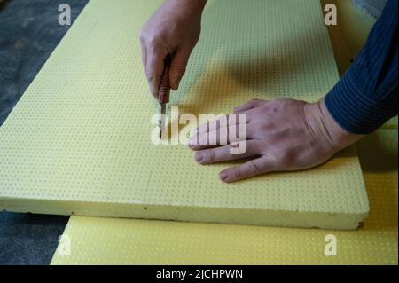 The master cuts expanded polystyrene on a floor, installation and warming of a floor in a room. Stock Photo