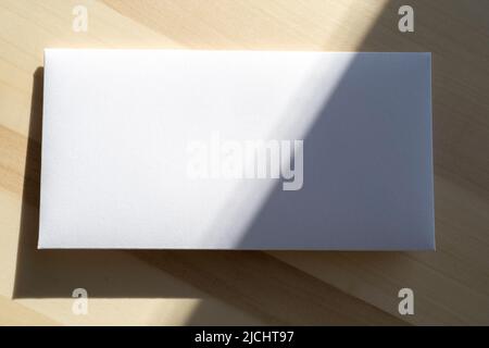 Blank white paper sheet, postcard, envelope as mockup and sunny light on surface Stock Photo
