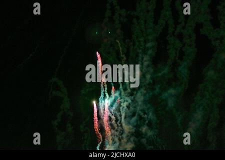 Flying up, bright volleys of fireworks, red, against the background of a greenish haze and the night sky. High quality photo Stock Photo