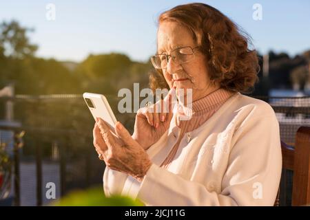 Caucasian elderly woman using a mobile phone outdoors. New technologies and senior citizens. Stock Photo