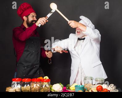 Two restaurant chefs or bakers in uniform fighting in kitchen. Cooking food. Competition of chef. Stock Photo