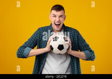 Millennial Man Holding Soccer Ball Shouting Emotionally Over Yellow Background Stock Photo