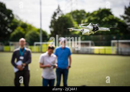 DJI Mini 3 Pro drone (UAV) in flight with pilots in background Stock Photo