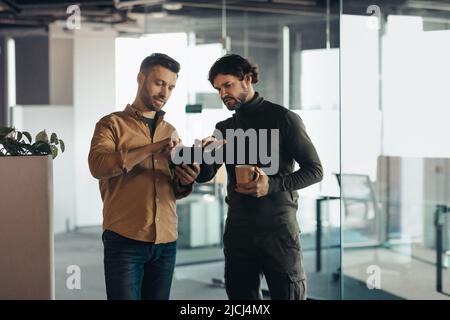 Portrait of focused colleagues using tablet pc, discussing business startup project, drinking coffee at company office Stock Photo