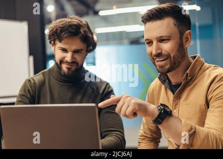 Positive male colleagues discussing business project, using laptop pc, brainstorming for ideas at office Stock Photo