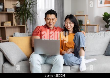 Loving chinese couple using laptop together, home interior Stock Photo