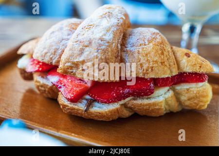 Fresh tasty croissant stuffed with sliced strawberries and cream, sprinkled with powdered sugar. Stock Photo