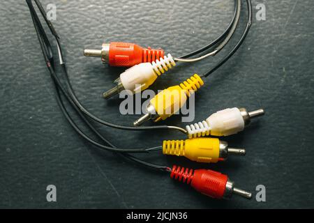 Wires with a triple double-sided plug tulip of the old generation close-up on a dark background. RCA connector Stock Photo