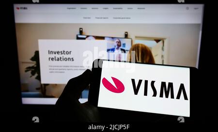 Person holding smartphone with logo of Norwegian software company Visma AS on screen in front of website. Focus on phone display. Stock Photo
