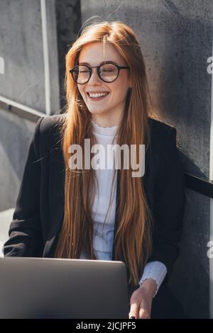 Smiling woman freelancer typing on computer keyboard and smiling, enjoying remote work while sitting on the bench in spring park. Business technology Stock Photo