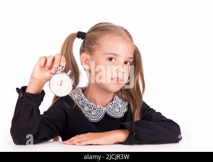 Little girl, blonde in a school dress points to a stopwatch on a white background Stock Photo