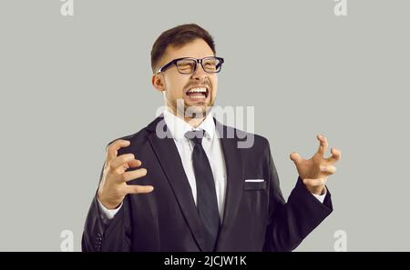 Crazy angry and frustrated young businessman shouting in anger isolated on gray background. Stock Photo