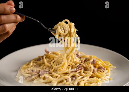 fork-is-spinning-carbonara-spaghetti-on-white-plate-on-a-black