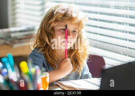 Tired serious schoolboy while doing homework. Portrait school kid siting on table doing homework. Funny child girl doing homework writing and reading Stock Photo