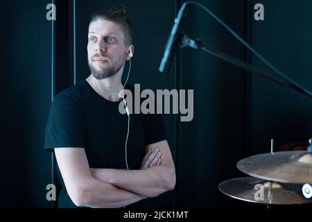 Portrait of a caucasian drummer in a black room of a recording studio behind a drum kit Stock Photo