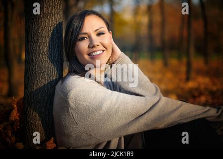 Young happy mixed race woman sitting on the grass in the park in autumn Stock Photo