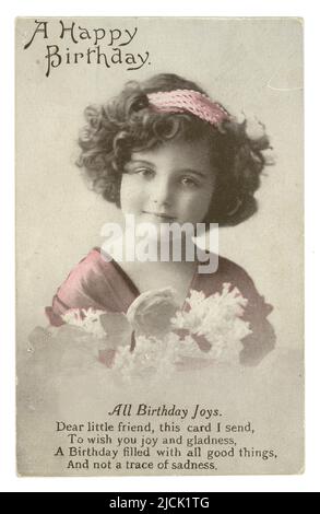 WW1 era sweet birthday greetings postcard wishing a friend a happy birthday. This tinted postcard is of a young girl, a regular model for these types of cards. She is wearing a headband and holding a bunch of flowers, poem on birthday joys, circa 1915, U.K. Stock Photo