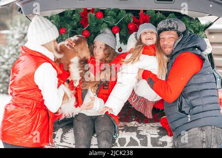 Happy winter moments for family with two children. Father, mother, girls spending time together with dog outdoors in car trunk with red Christmas Stock Photo