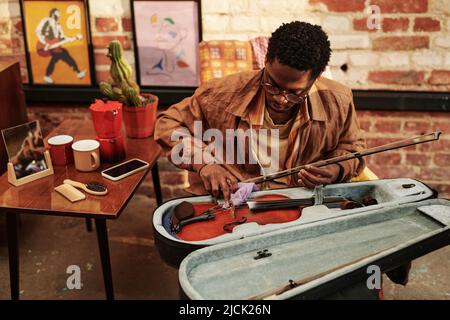 Young black man skilled in playing violin opening slipcover with musical instrument and taking it out while going to perform piece of music Stock Photo