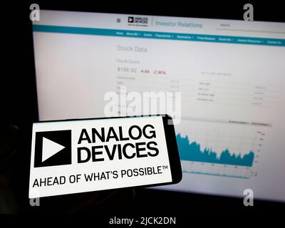 Person holding mobile phone with logo of semiconductor company Analog Devices Inc. (ADI) on screen in front of web page. Focus on phone display. Stock Photo