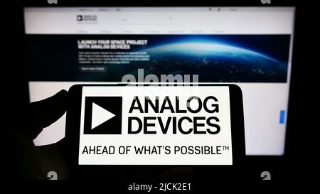 Person holding cellphone with logo of semiconductor company Analog Devices Inc. (ADI) on screen in front of webpage. Focus on phone display. Stock Photo