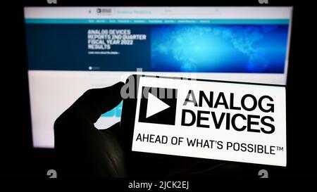 Person holding smartphone with logo of semiconductor company Analog Devices Inc. (ADI) on screen in front of website. Focus on phone display. Stock Photo