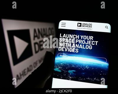 Person holding cellphone with website of semiconductor company Analog Devices Inc. (ADI) on screen with logo. Focus on center of phone display. Stock Photo