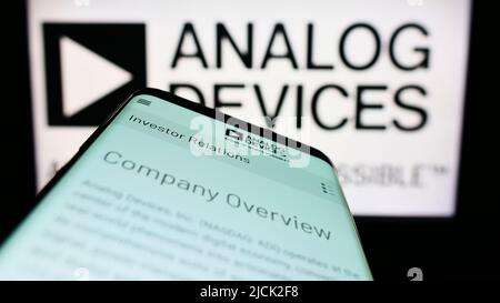 Smartphone with webpage of semiconductor company Analog Devices Inc. (ADI) on screen in front of logo. Focus on top-left of phone display. Stock Photo