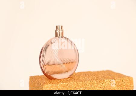 Unbranded round glass perfume bottle on golden podium on ivory background. Eau de toilette. Mockup, copy space Stock Photo