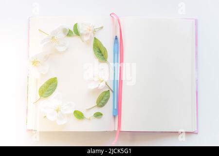 Open book with white sheets and a blue pen in apple blossoms around. Stock Photo