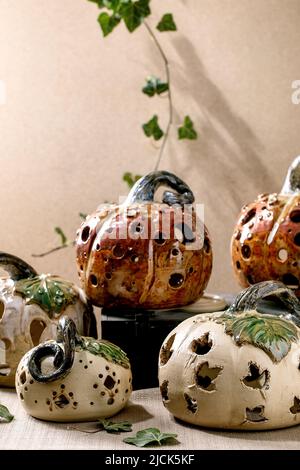 Halloween decorations, set of white and brown handcrafted carved ceramic pumpkins standing on table with ivy leaves. Halloween or Thanksgiving holiday Stock Photo