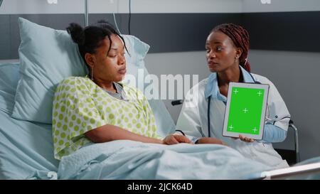 Medical specialist vertically holding green screen on tablet in hospital ward. Physician and sick person looking at gadget display with chroma key and isolated mockup background. Stock Photo