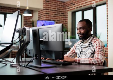 Confident creative office worker sitting at computer in office workspace while developing digital art. Professional employee graphics designer sitting at desk while working on project. Stock Photo