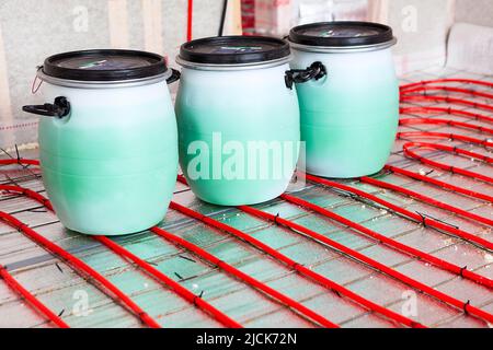 Underfloor heating system installation. Interior of a new residential building. Pipes filled with propylene glycol from cans. Individual heating Stock Photo