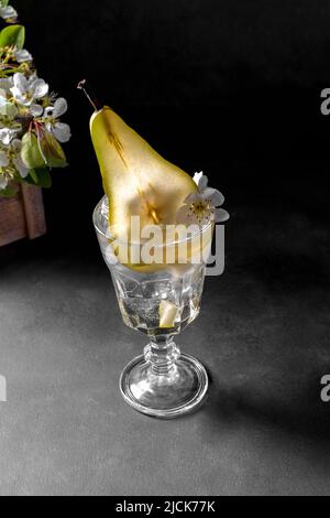 Pear cocktail in a glass decorated with fresh fruit and flowers on dark gray background. Summer cold pear drink lemonade with ice on the table, Sparkl Stock Photo