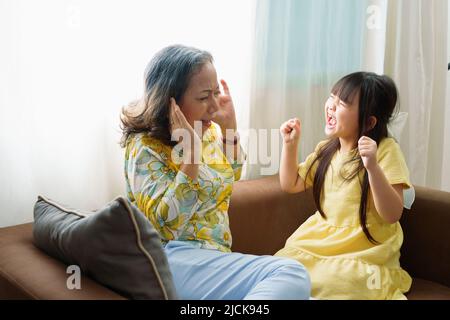 Asian portrait, granddaughter expressing displeasure by yelling at grandmother covering her ears, aggression, violence, upbringing Stock Photo