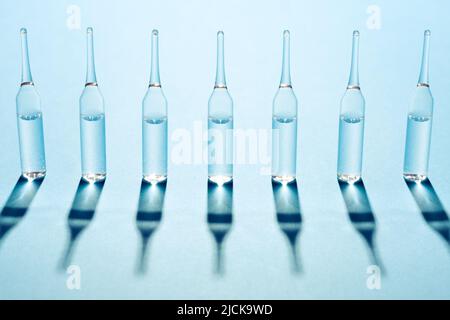 Seven ampules under the bright light on blue background. Stock Photo