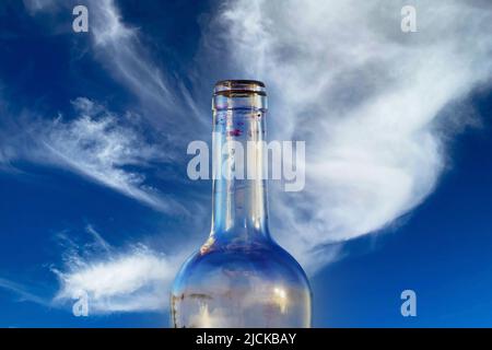 Closeup of one single isolated empty transparent red wine alcohol glass bottle, clear blue sky and fluffy white cloud background Stock Photo