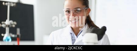Pretty cheerful laboratory worker in medical gown examine sample under microscope Stock Photo