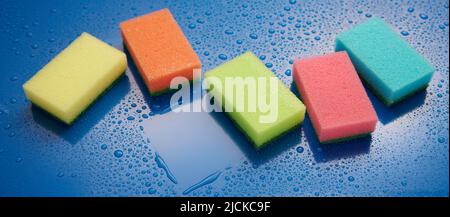 From above of various colorful sponges for dishwashing placed on wet blue background with water drops during household routine in room Stock Photo