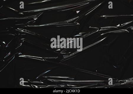 Crumpled wrinkled plastic cellophane. Transparent plastic wrap on black background. Reflecting light and shadow on creases and folds in plastic Stock Photo