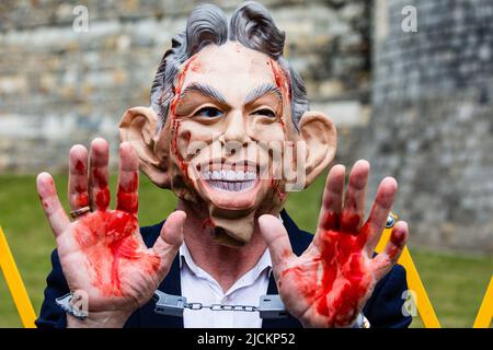 Windsor, UK. 13th June, 2022. A Stop the War Coalition activist wearing a Tony Blair mask and with hands daubed with fake blood protests outside Windsor Castle against the awarding of a knighthood to former Prime Minister Sir Anthony Blair following his controversial role in the Iraq War. Sir Anthony Blair was knighted during a private audience with the Queen last week and is being installed as a member of the Order of the Garter during a ceremony at Windsor Castle. Credit: Mark Kerrison/Alamy Live News